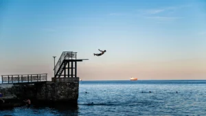 Silhouette of swimmer jumping off seaside pier with ship on horizon
