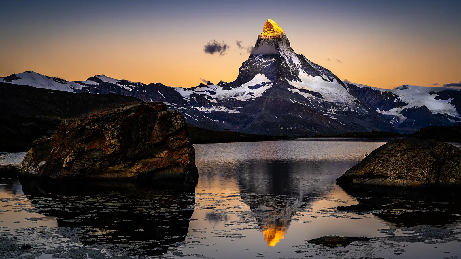 Golden sunrise lighting the Matterhorn with snowy ridges mirrored in mountain lake