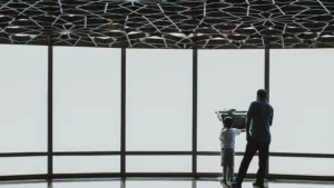 Man and young boy looking out tall glass windows under patterned ceiling