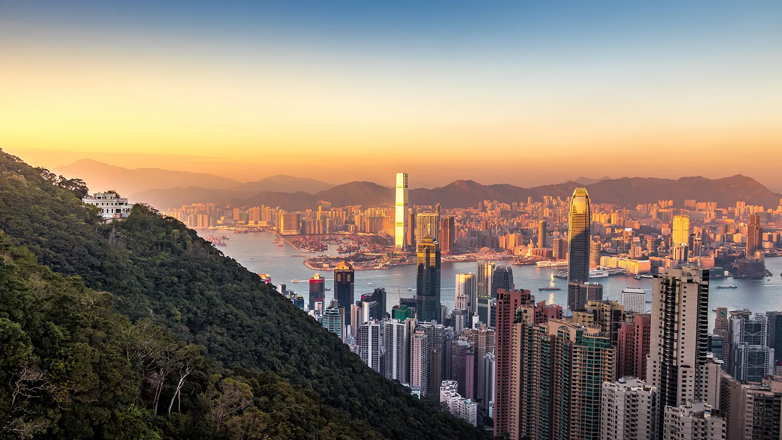 High-rise buildings along Victoria Harbour with hills and warm evening sky