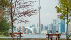 People sitting on park benches overlooking Toronto skyline with CN Tower across water