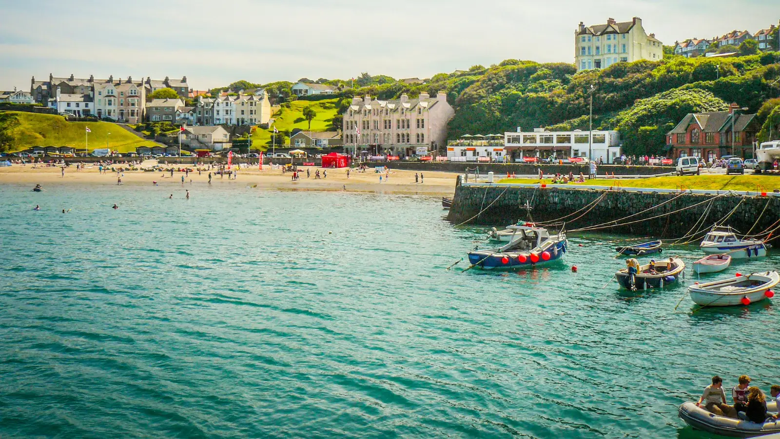 Isle of Man harbor scene with anchored boats, beachgoers, and hillside homes