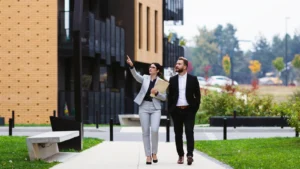 Two professionals walking past modern apartment buildings, woman pointing ahead