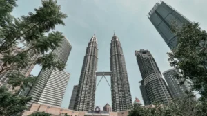Kuala Lumpur cityscape featuring Petronas Twin Towers framed by nearby glass skyscrapers and trees