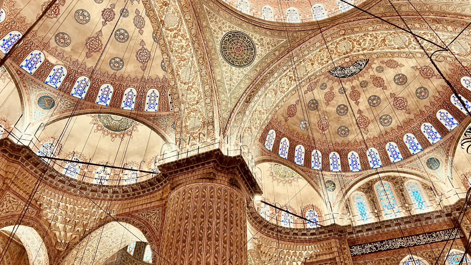 Grand Ottoman mosque ceiling featuring detailed motifs, curved arches, and bright stained-glass windows