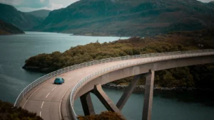 Curved concrete bridge over fjord with small car and mountainous landscape