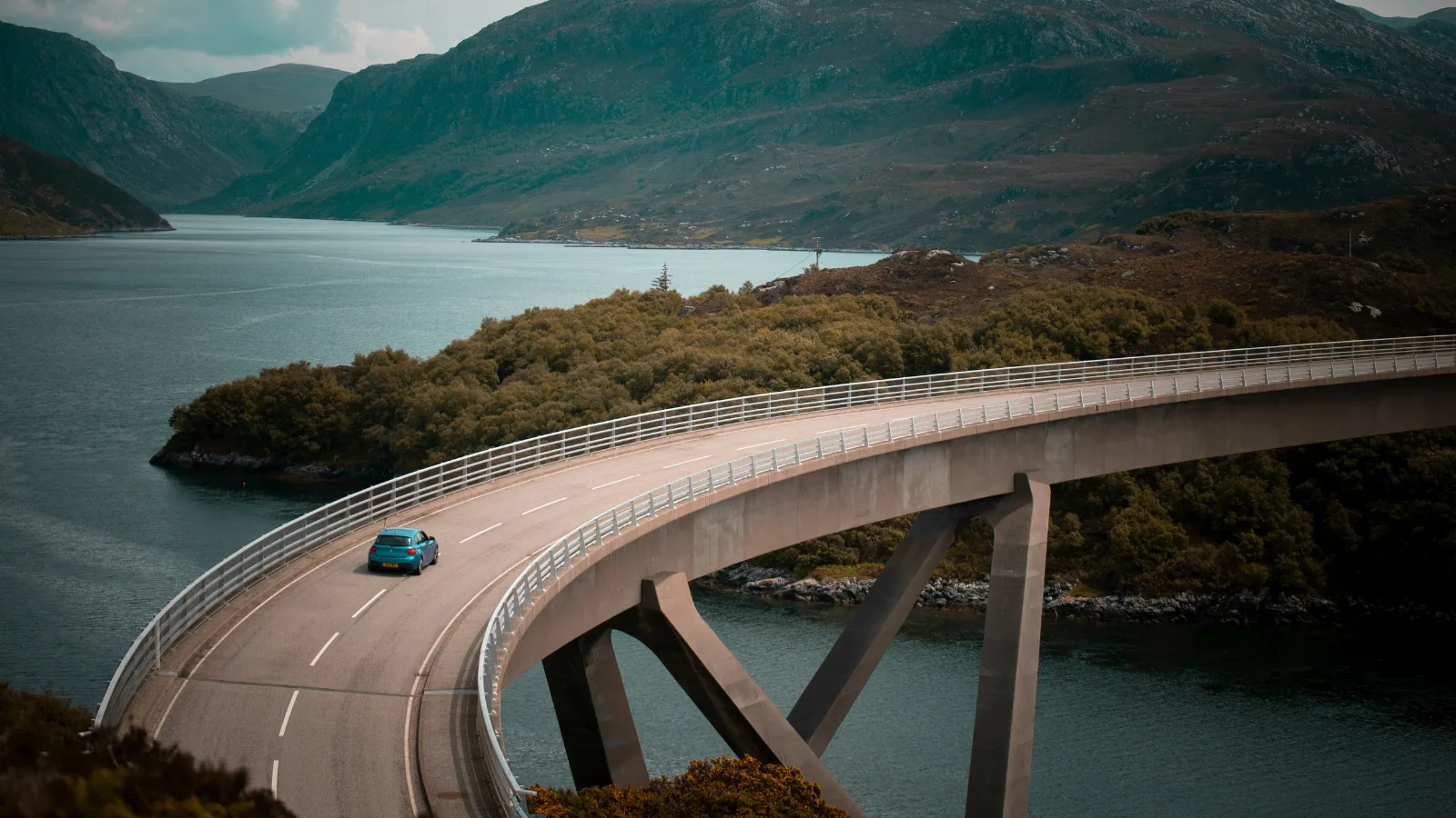 Curved concrete bridge over fjord with small car and mountainous landscape