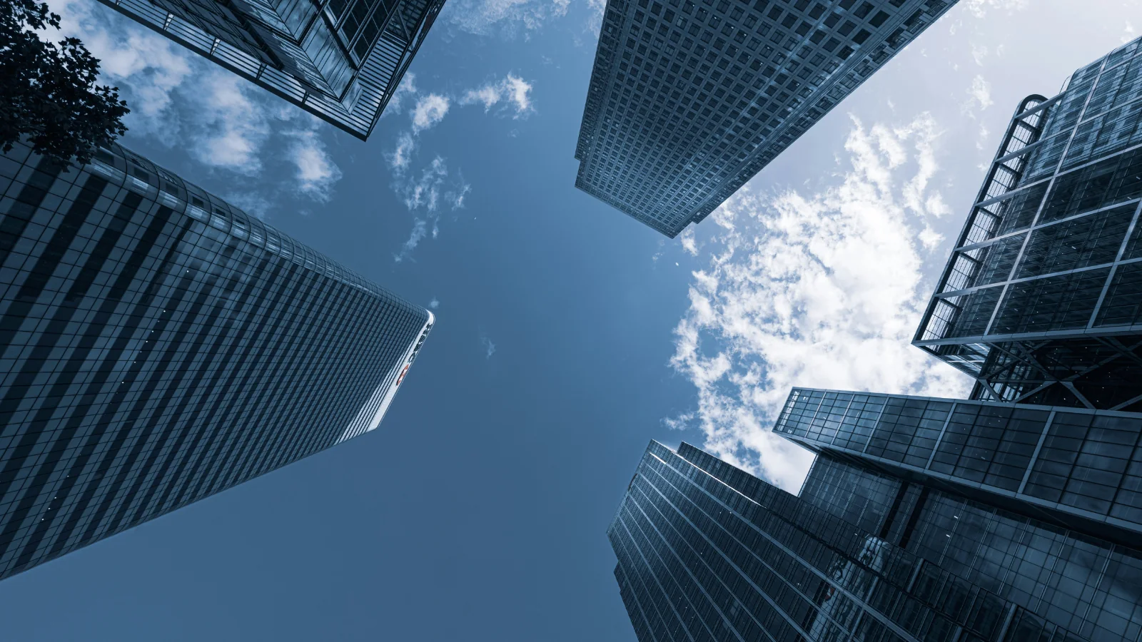 Upward view of modern glass skyscrapers surrounding blue sky with scattered clouds