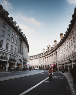 Cyclist riding along Regent Street's curved facade with a red bus and shoppers nearby