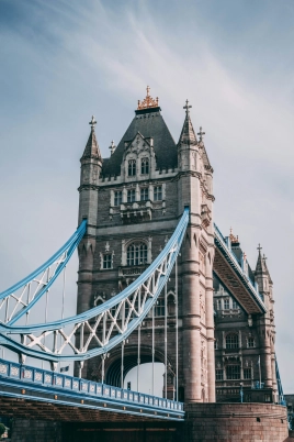 Wide angle view of Tower Bridge's Gothic towers and blue suspension trusses against a cloudy sky