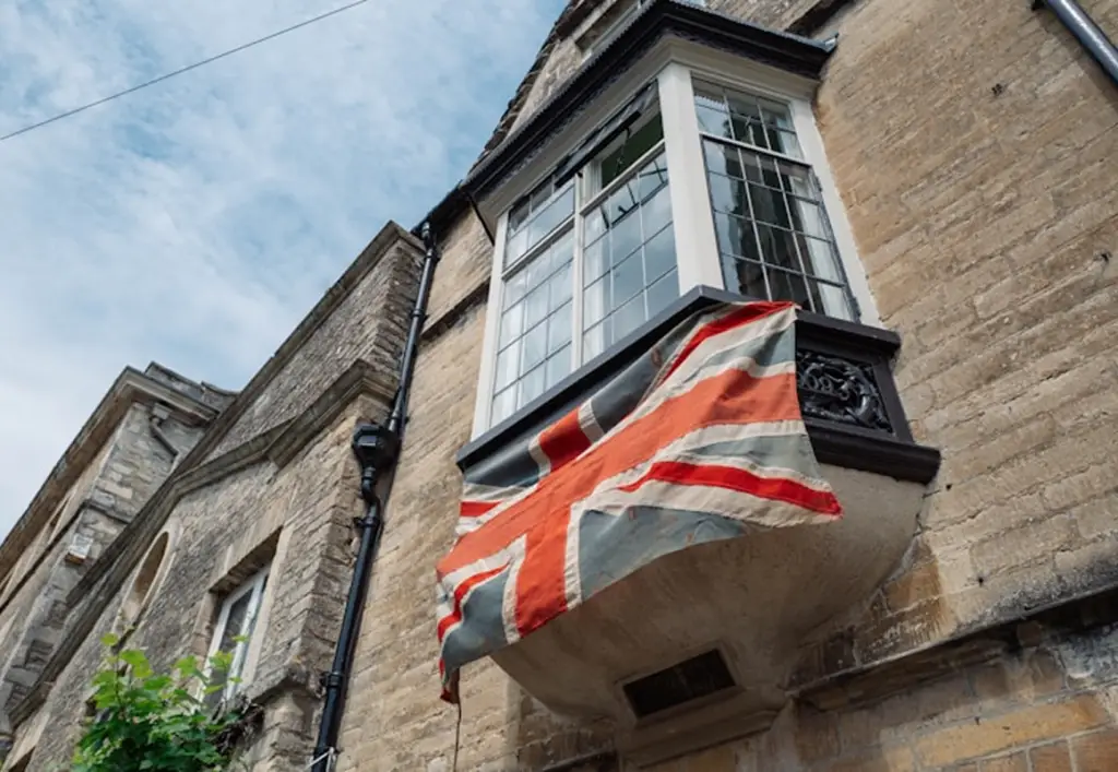 Union Jack flag hanging from a bay window balcony on a traditional British stone building