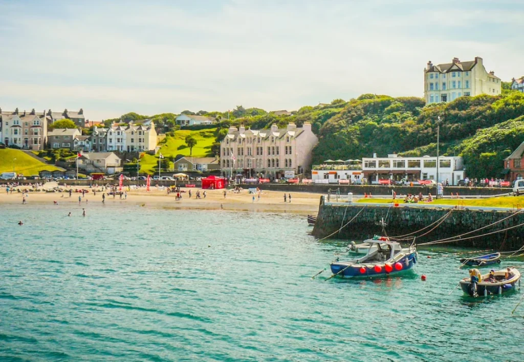 Coastal town with a sandy beach, small boats and clifftop houses beside turquoise water