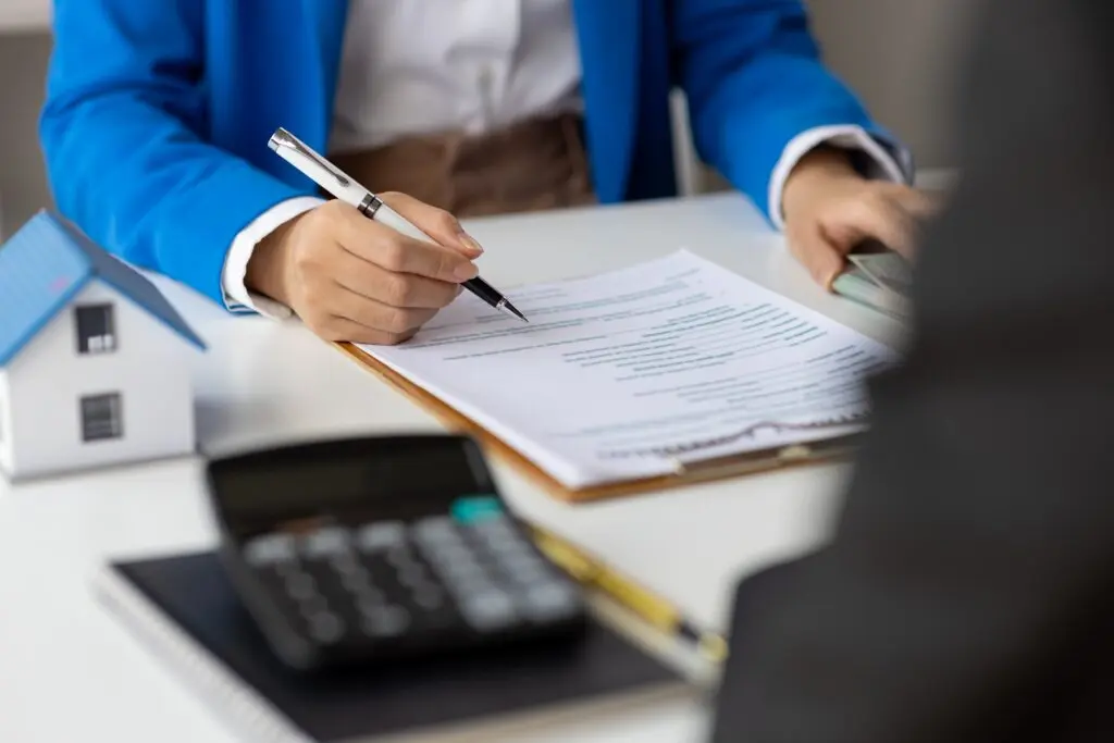 Woman in a blue blazer signing a buy-to-let mortgage agreement, with a model house and calculator on the desk