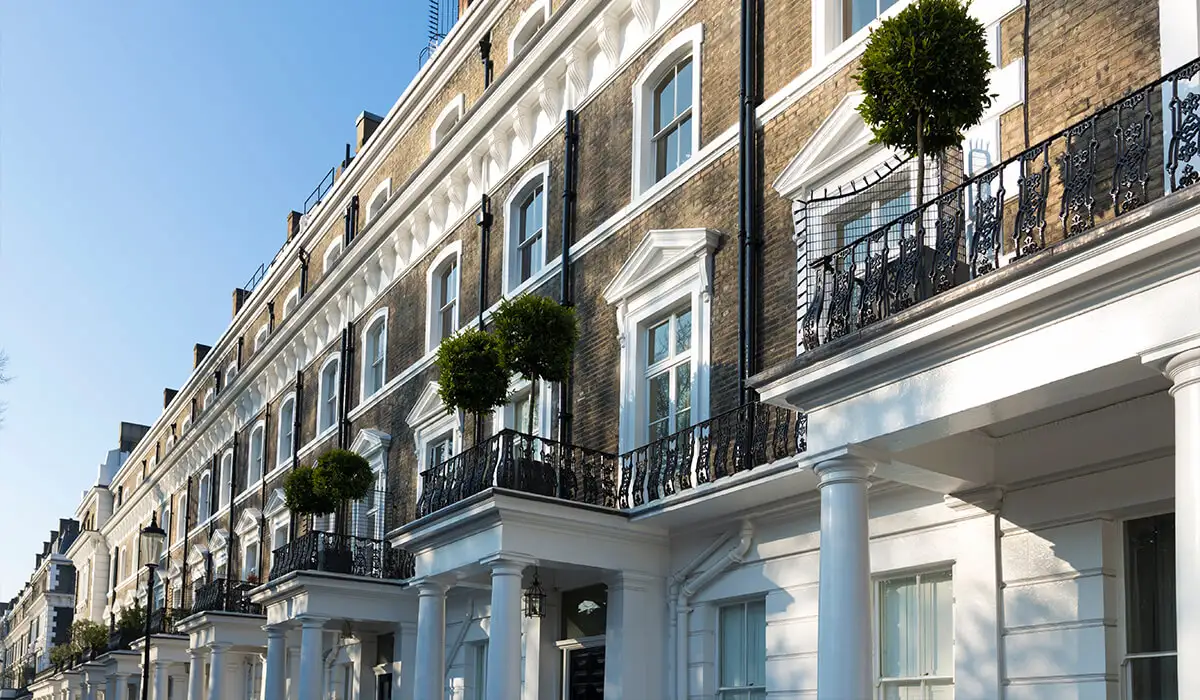 Row of white period London townhouses with black wrought-iron balconies and topiary trees under a clear blue sky