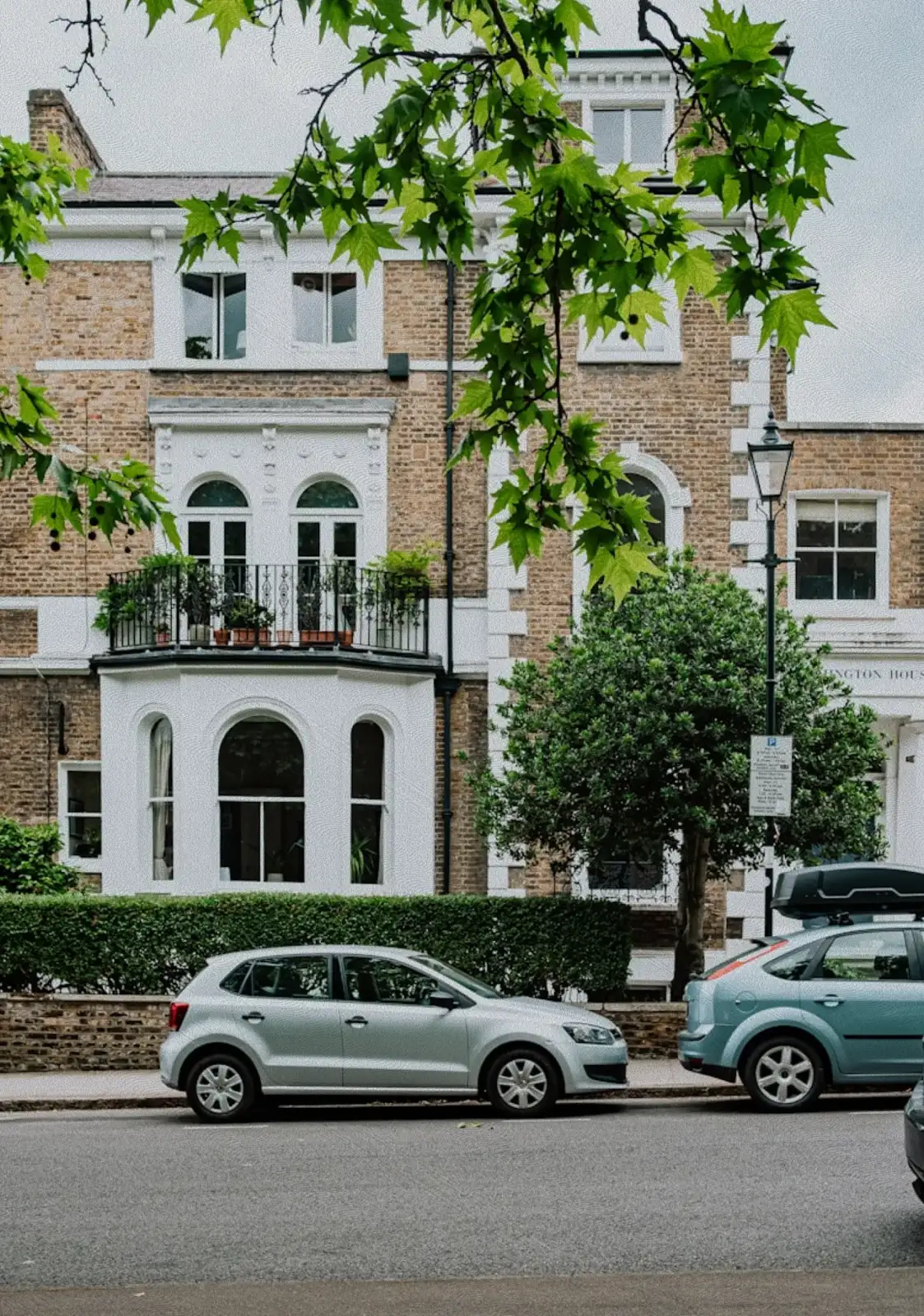 Victorian brick townhouse on a London street with cars parked outside and a tree overhead