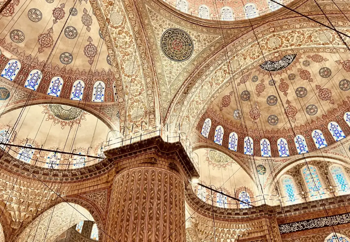 Ornately tiled blue domed ceiling with arched windows inside a mosque