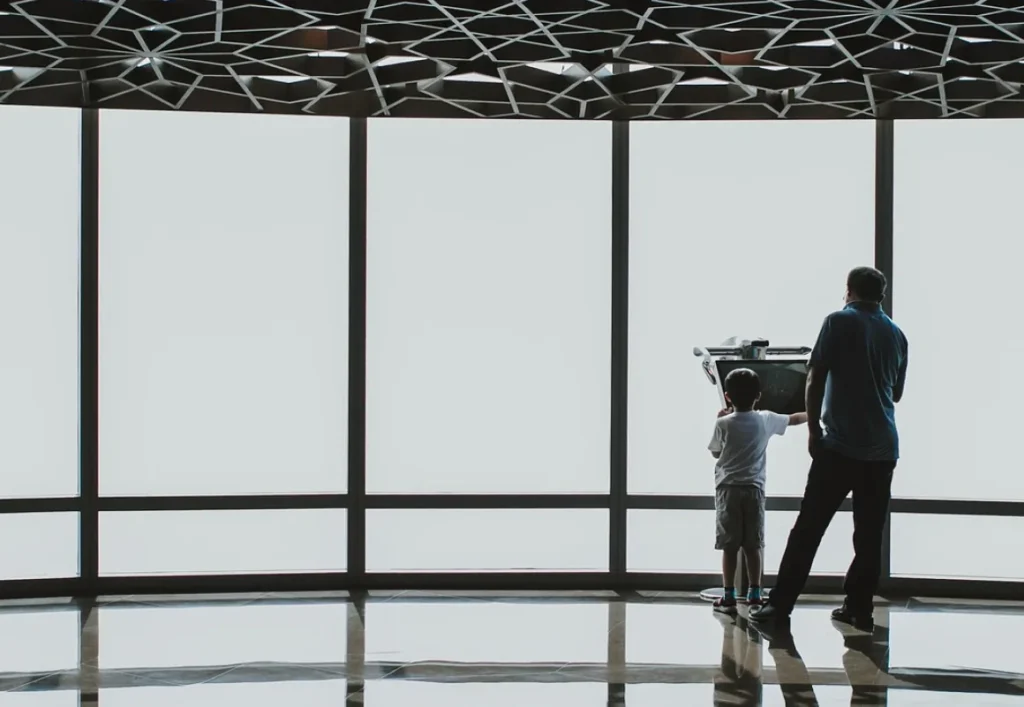 Adult and child looking out through a glass facade beneath a perforated dome canopy in the UAE