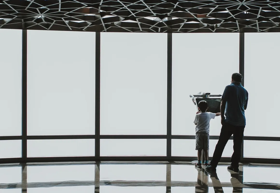 Adult and child looking out through a glass facade beneath a perforated dome canopy in the UAE