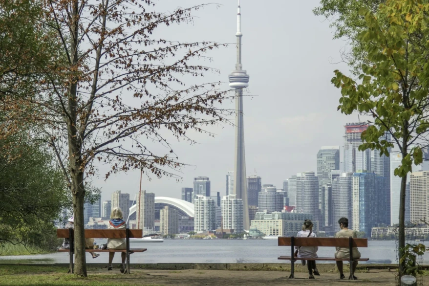 People relaxing on park benches by the water with the Toronto skyline and CN Tower behind