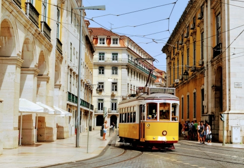 Yellow tram number 25 travelling through a historic Lisbon street lined with period buildings
