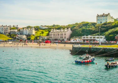 Coastal town with a sandy beach, small boats and clifftop houses beside turquoise water