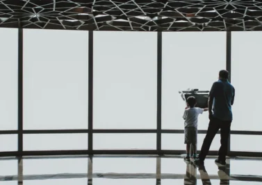 Adult and child looking out through a glass facade beneath a perforated dome canopy in the UAE
